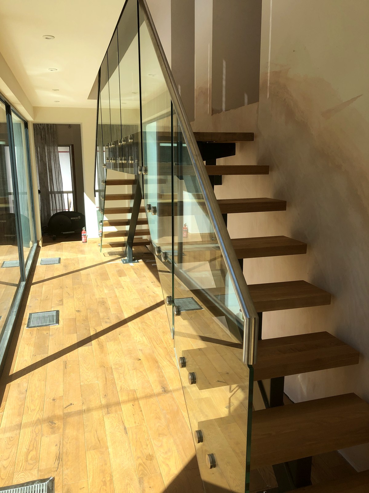 Solid oak treads cantilevered off an anthracite grey steel spine with a glass balustrade, Surrey