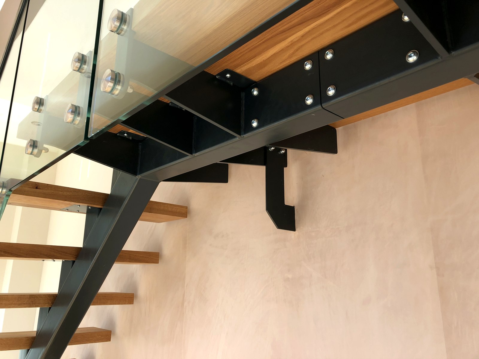 Slotted stainless steel handrail and steel spine connection detail on an oak and glass staircase, Surrey