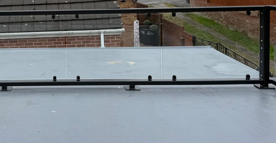 Balustrade bottom rail held clear of the roof covering on flat bar bearing feet