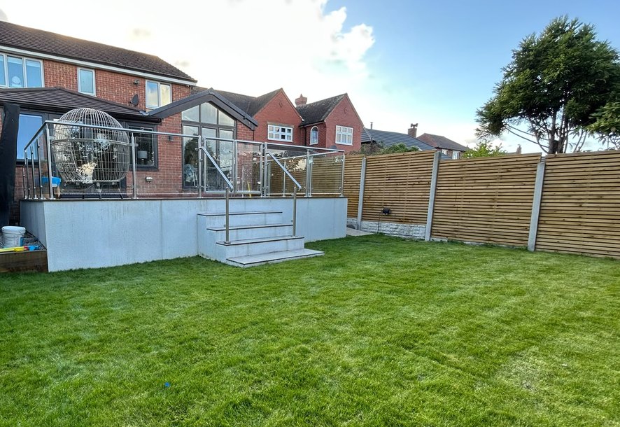 Raised patio with a stainless steel and glass balustrade and steps down to the lawn, Rotherham