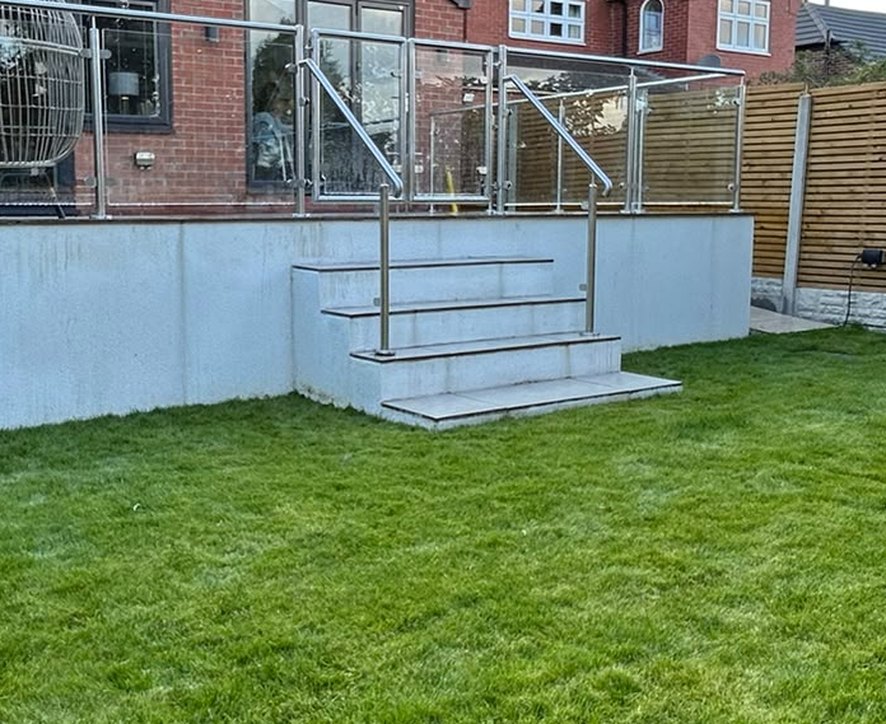 Stainless steel raking handrails either side of masonry steps from a raised patio down to the lawn
