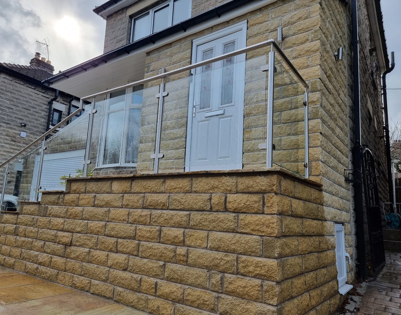 Framed glass balustrade in satin stainless steel guarding a raised stone entrance terrace in Sheffield