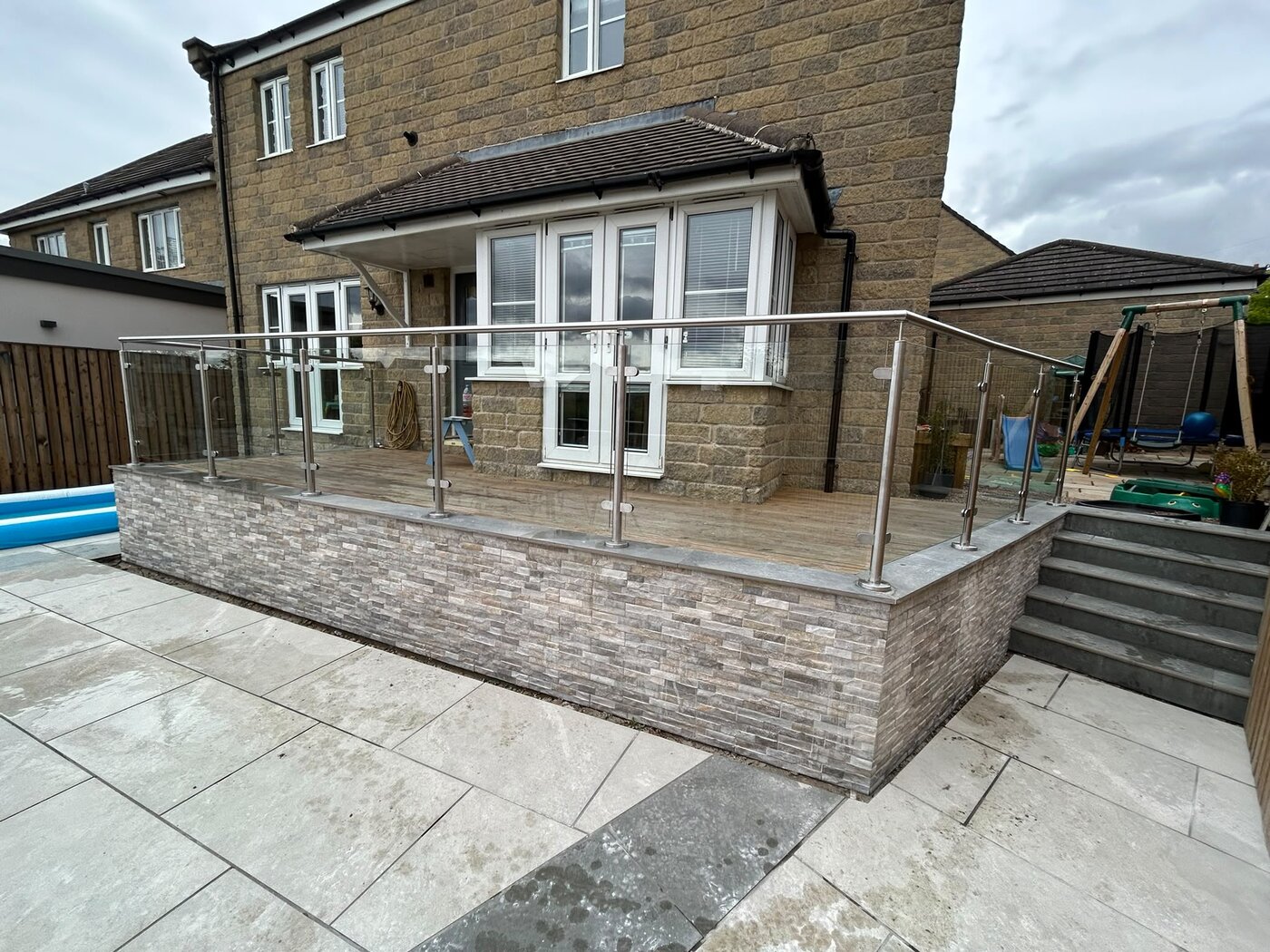 System 1 stainless steel and glass balustrade around a raised patio with a stone clad retaining wall, Rotherham