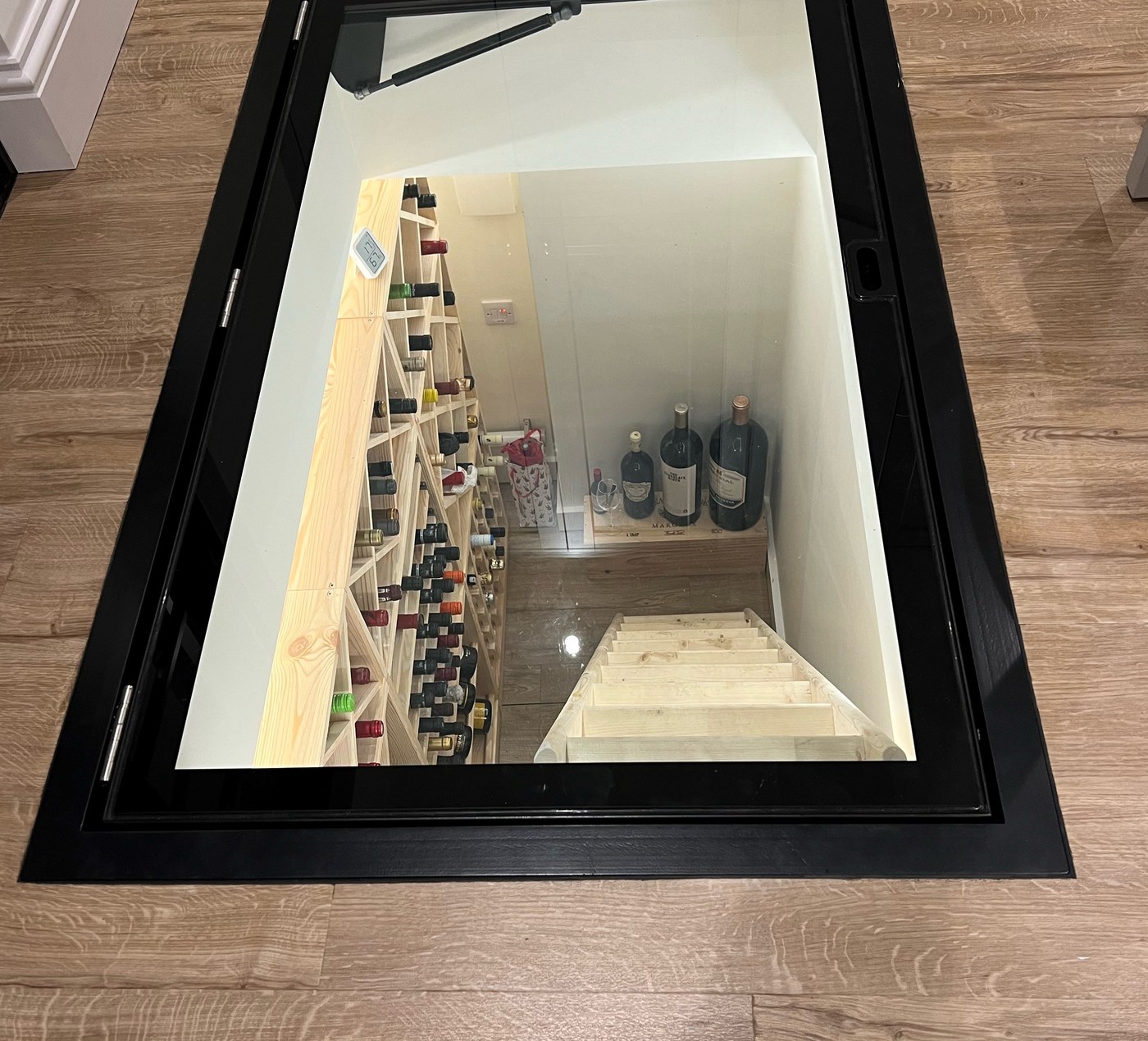 Hinged glass wine cellar door set into a timber floor, looking down into a converted coal store