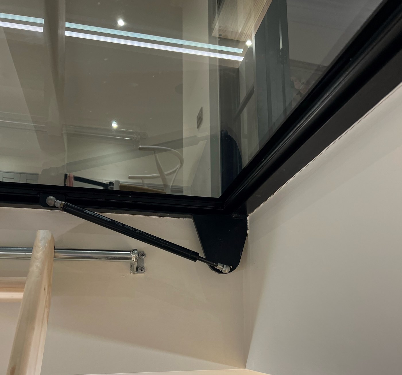 Underside of a walk-on glass floor hatch showing the gas strut and steel frame from inside the cellar