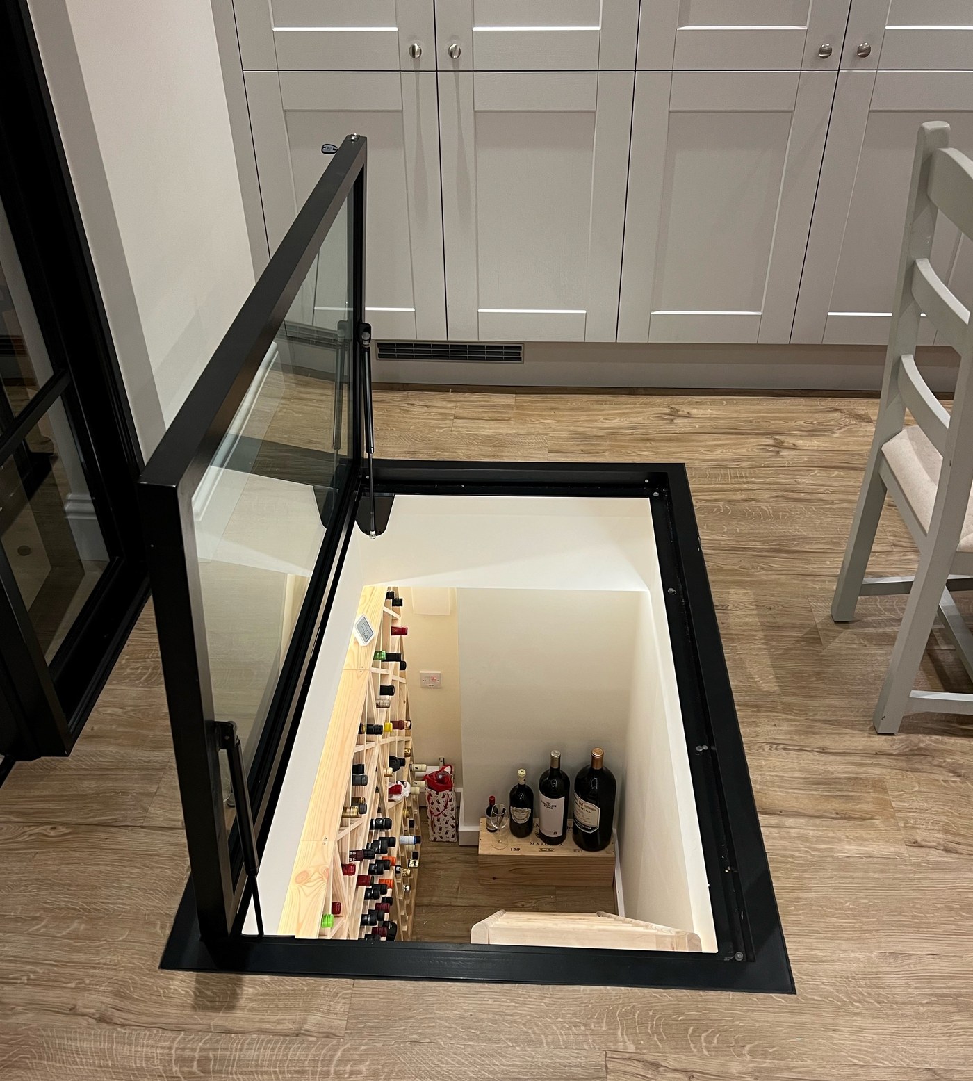 Gas strut glass floor hatch held open above a wine cellar in a kitchen