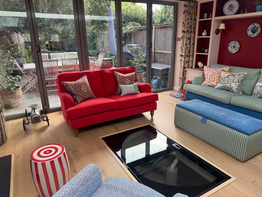Glass cellar door set into the floor of a furnished living room with sofas either side and doors to the garden