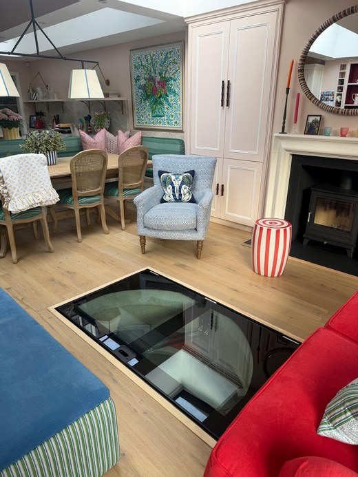 Glass cellar door in a London living room with a wood burning stove and dining area beyond