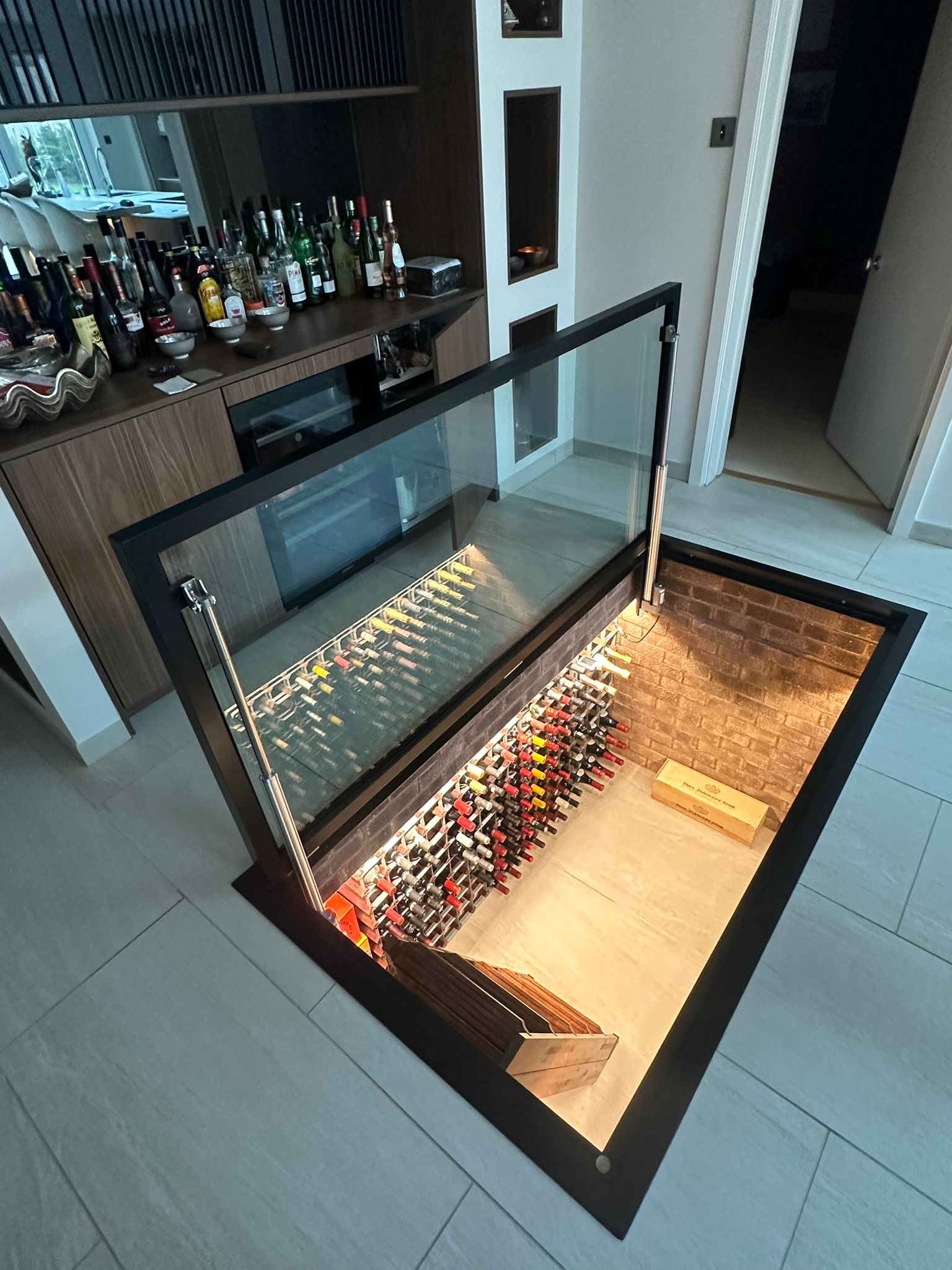 Electric glass floor hatch open over a wine cellar, showing the open void and racking below