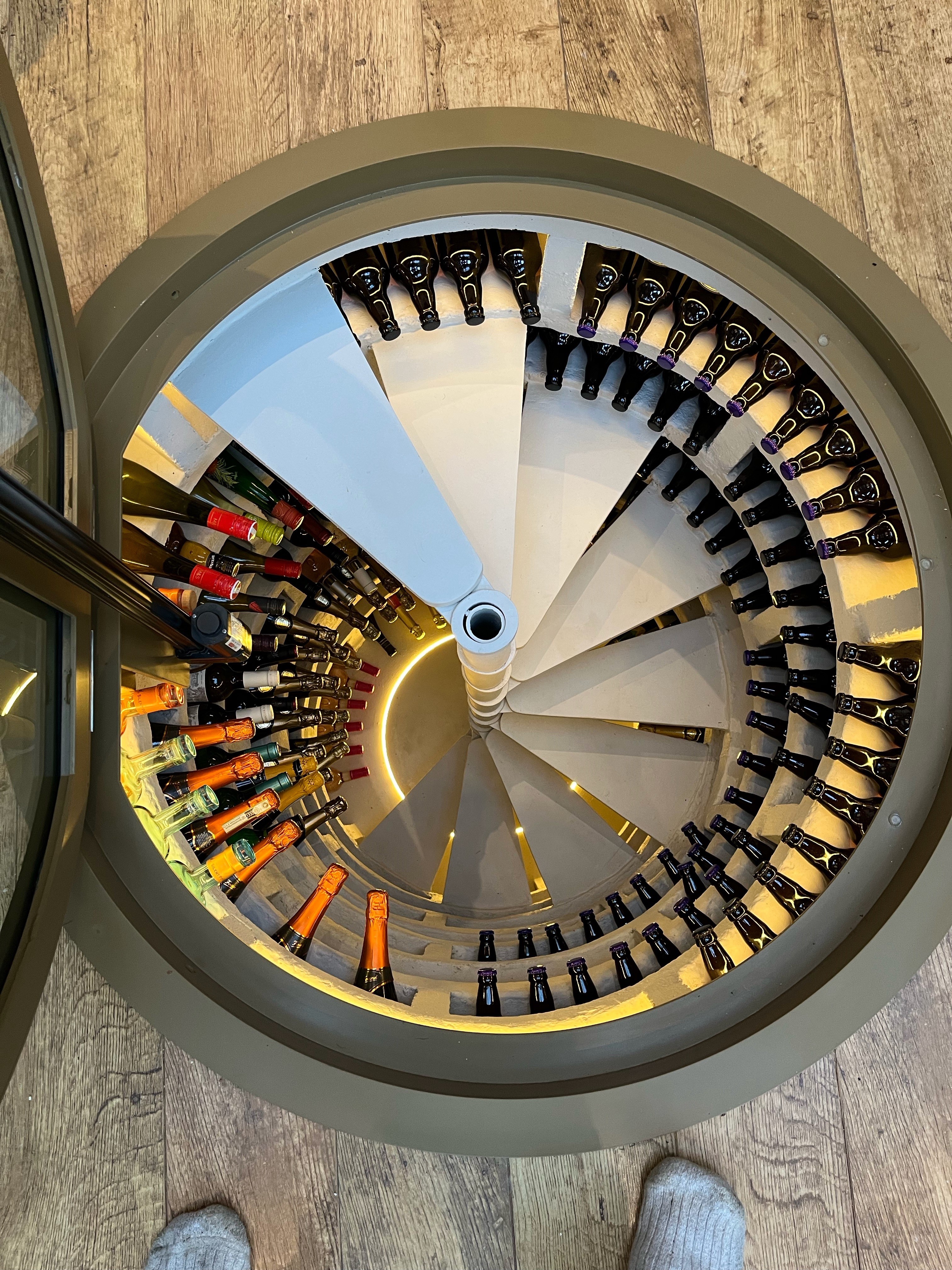 Circular electric glass hatch over a spiral wine cellar staircase, open to show the steps below