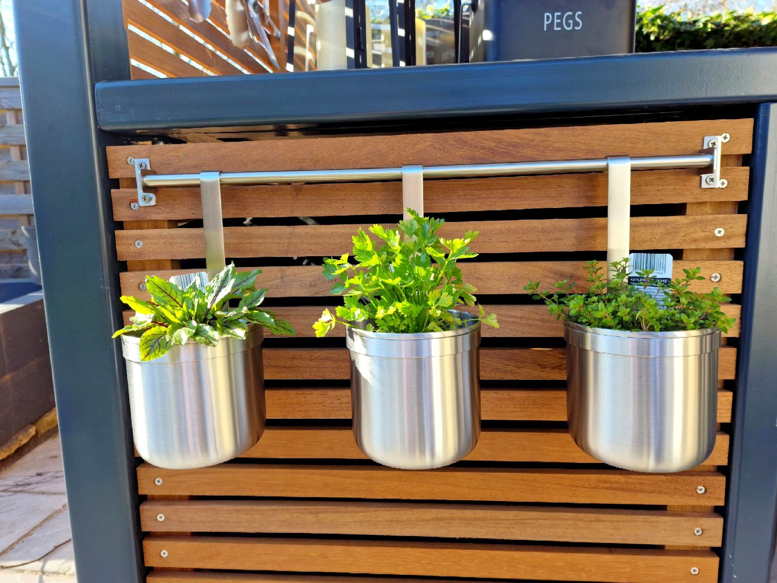 Iroko-slatted pergola panel with stainless steel hanging planters on a drilled-and-tapped rail