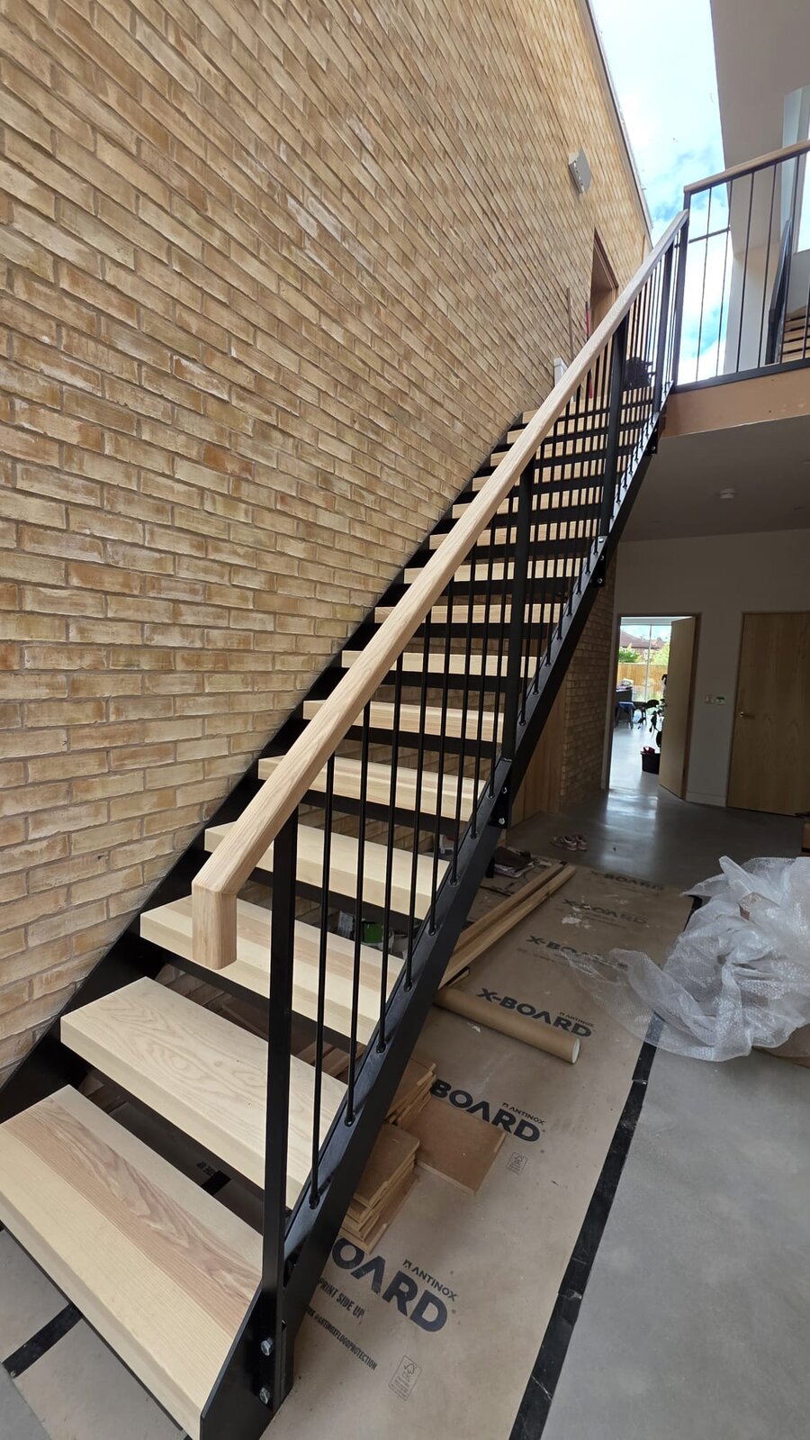 Steel staircase with solid ash treads and black powder coated metal balustrade against a brick wall, Chorlton Manchester