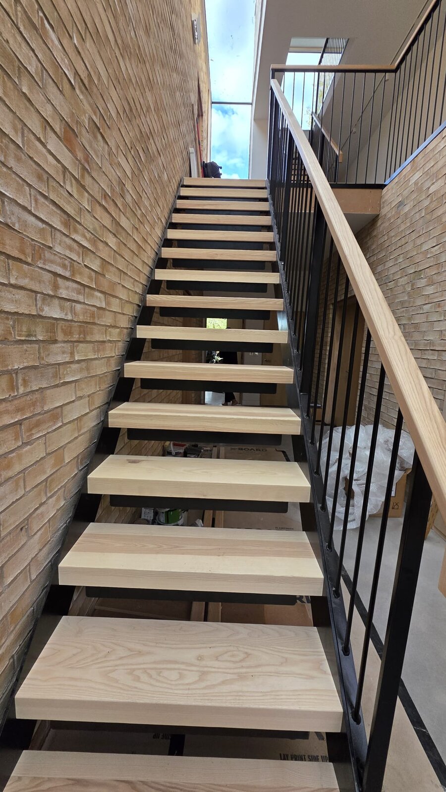 Open riser steel stair with pale ash treads rising against exposed brickwork, Manchester