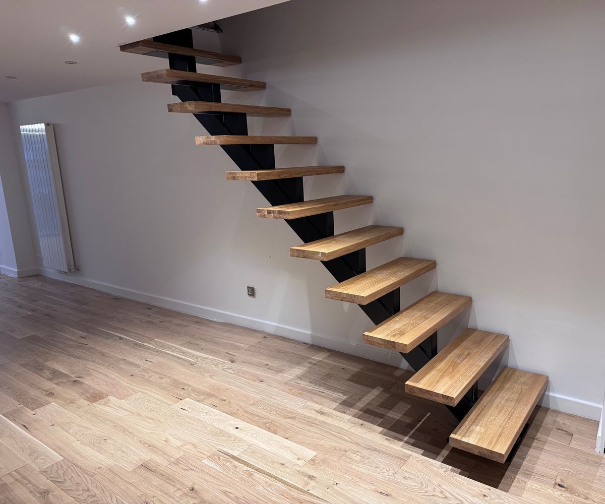Side view of a mono stringer spine staircase in black powder coated steel with oak treads, London SE8