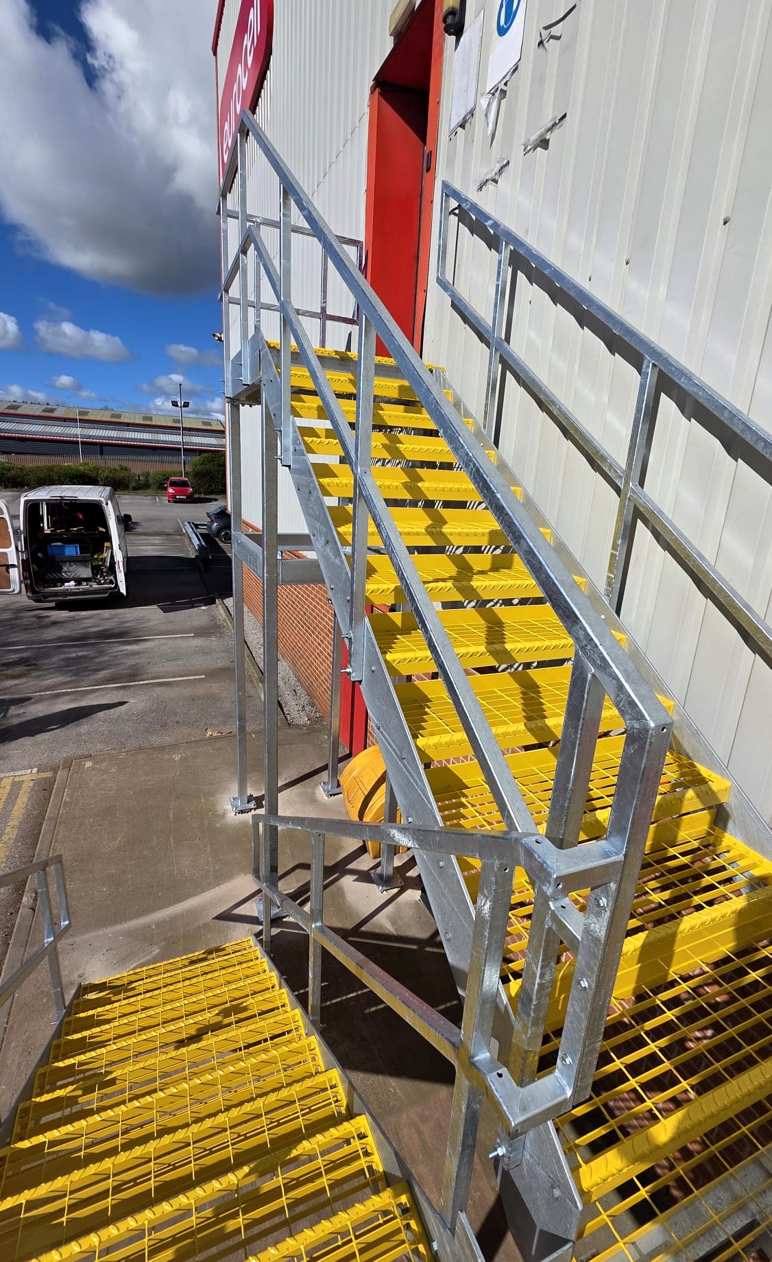 Galvanised steel fire escape staircase with yellow powder-coated open mesh flooring treads and twin handrail, detail view Eurocell Alfreton