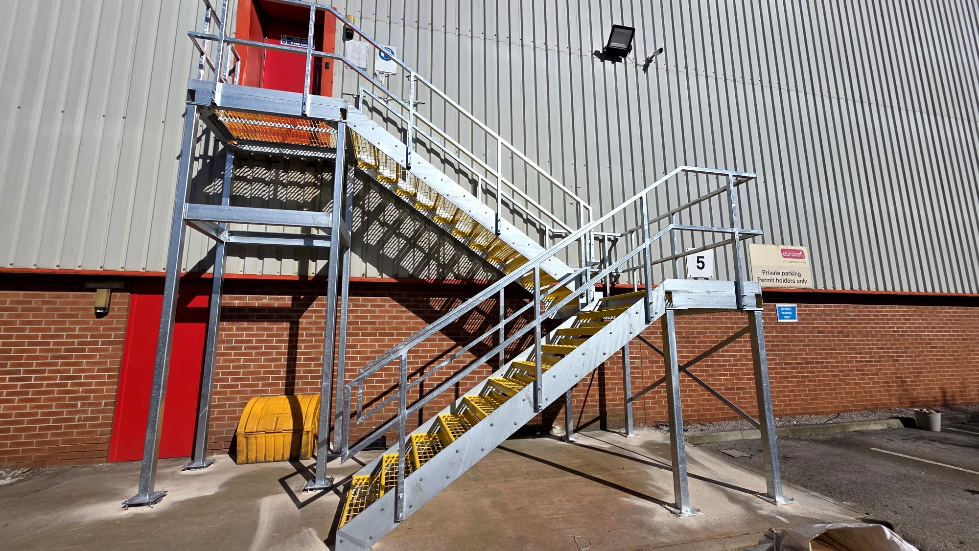 Full galvanised steel fire escape staircase structure at Eurocell Alfreton with intermediate landing and braced support frame