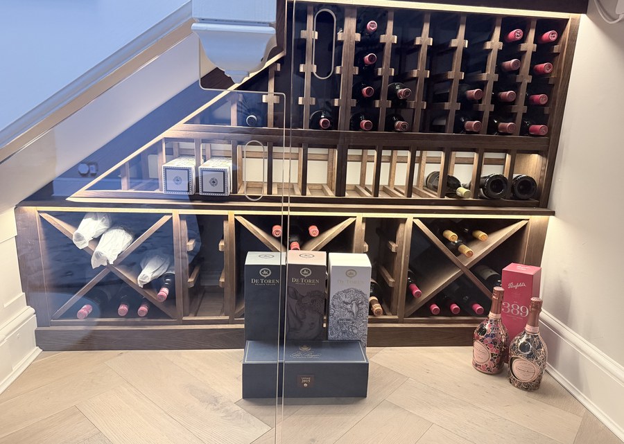 Frameless toughened glass doors closing in a lit under stairs wine store with oak racking in Warrington