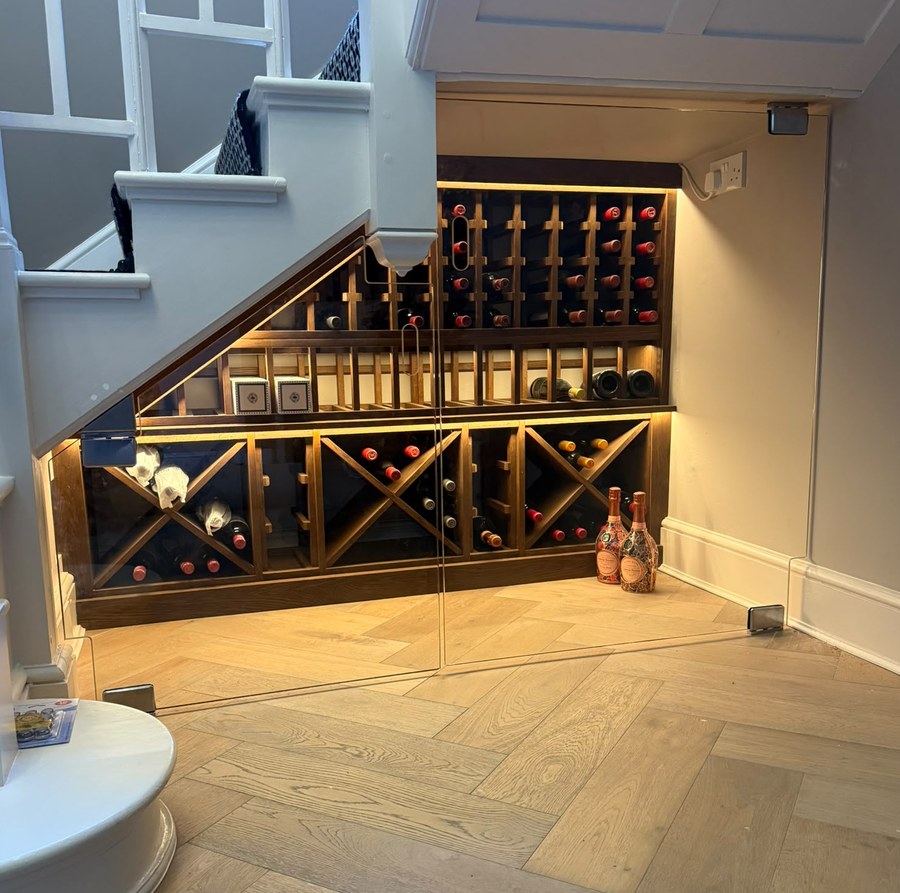 Glass doors cut to the rake of the staircase above a stained oak wine rack