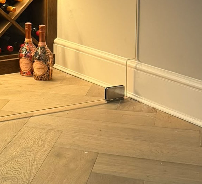 Brushed stainless steel patch hinge at floor level with the glass notched over the skirting board