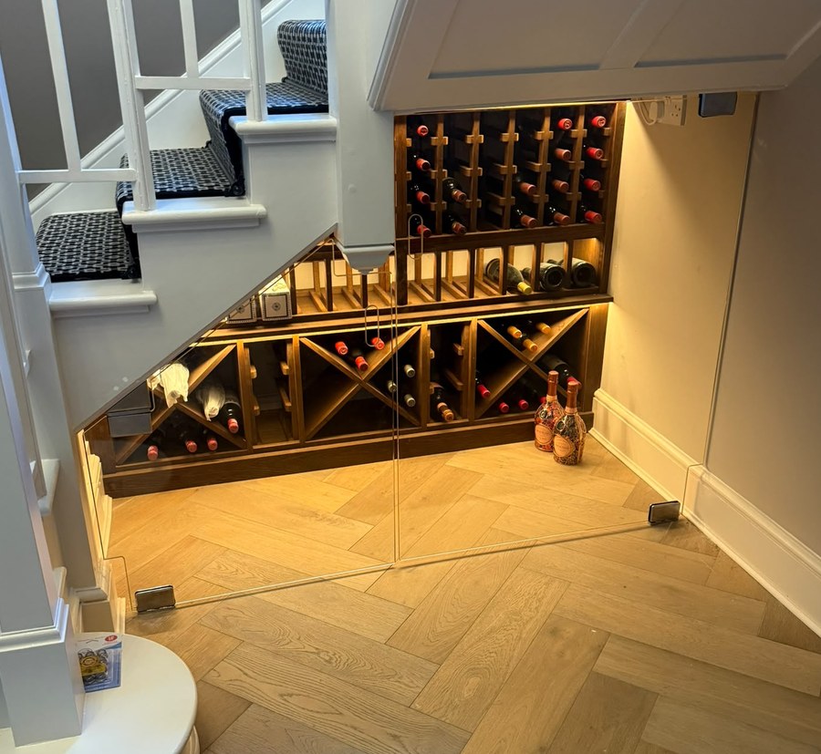 Lit stained oak wine racking with diamond bins seen through frameless glass doors