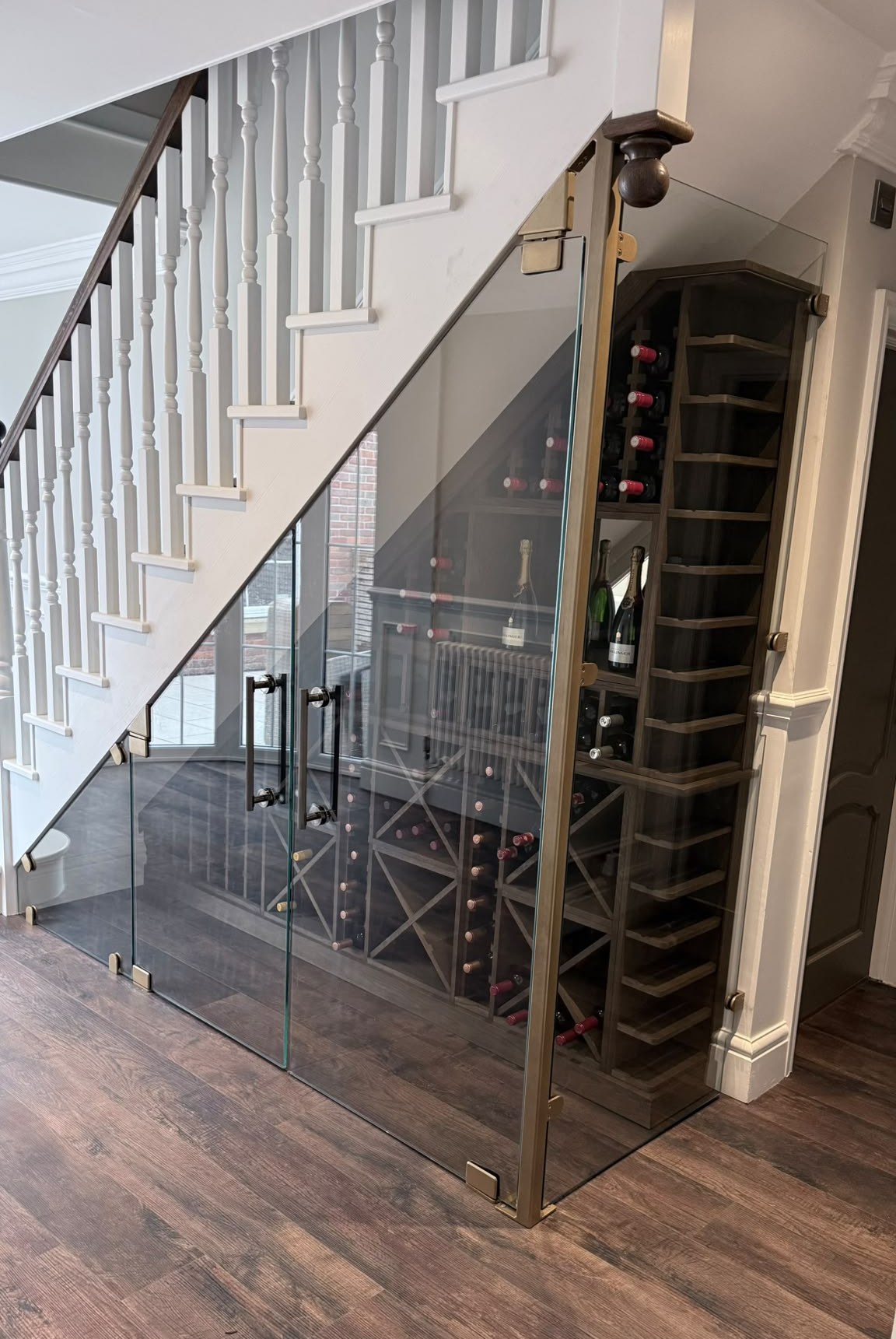 Raked glass doors cut to the stair soffit with matt black pull handles and gold powder coated clamps