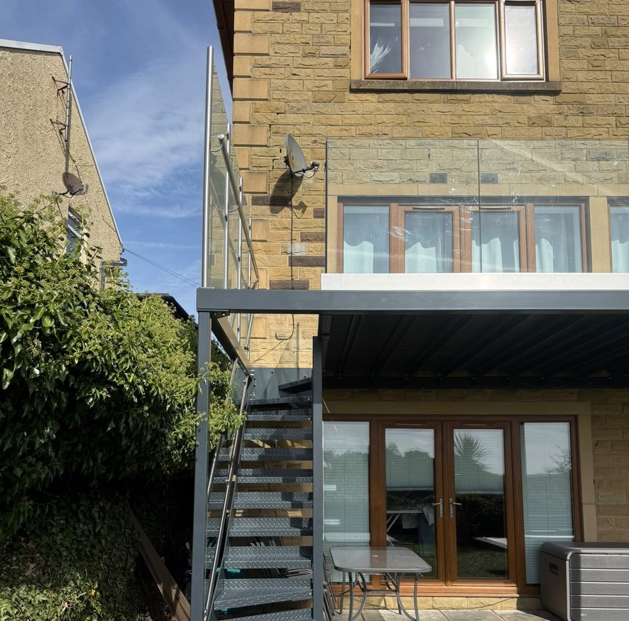 External steel staircase with glass balustrade running from the balcony down to the garden