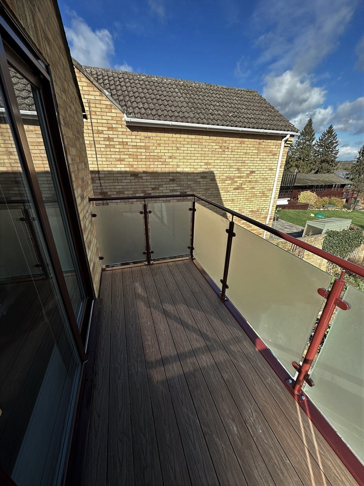 Obscure privacy glass balustrade and dark brown composite decking on a first floor walkout balcony